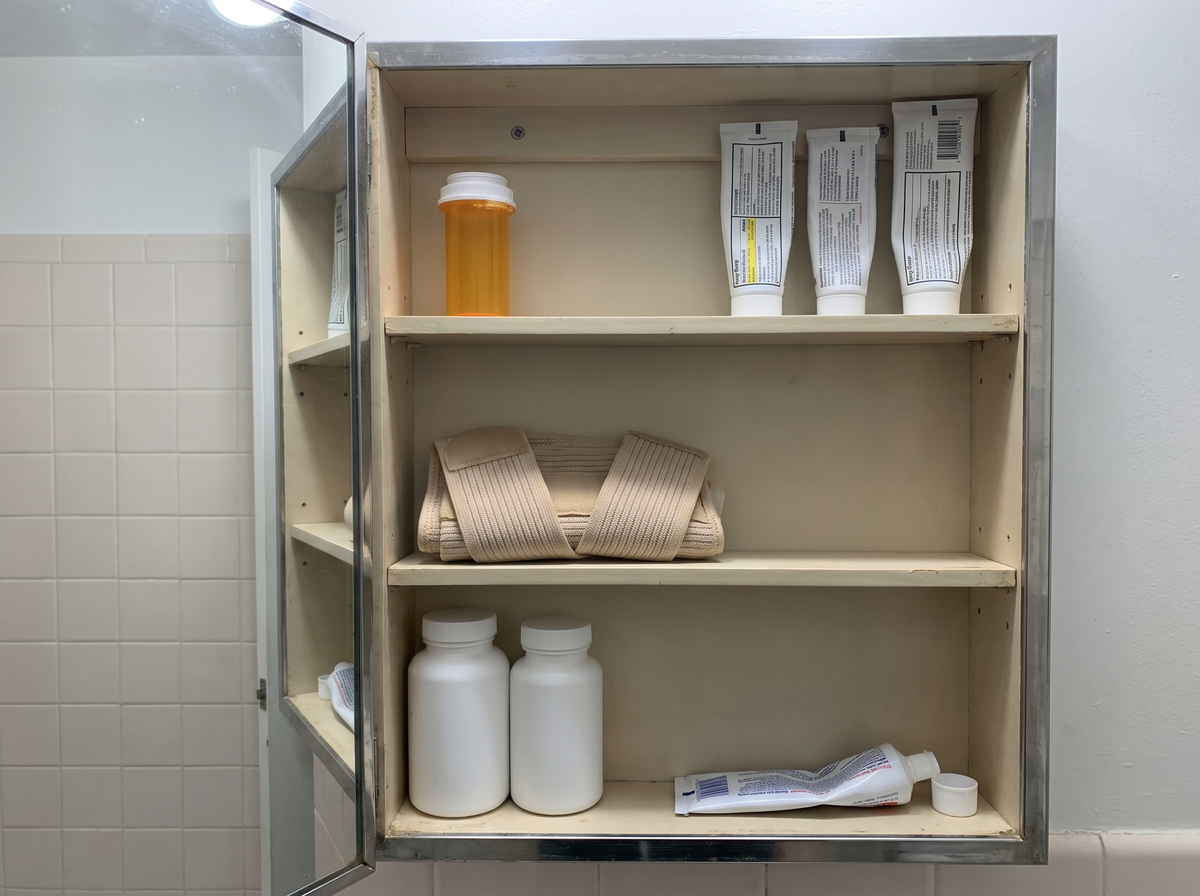 The bathroom cabinet: tablets, creams, a wrist support, bottles turned to the wall.